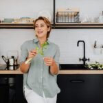 Smiling woman with vegetables in a stylish kitchen showcasing modern interior design.